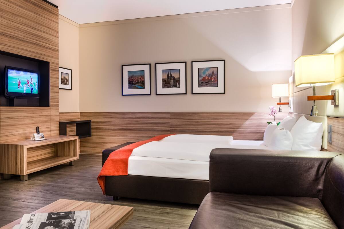 Une chambre d’hôtel avec un lit, une télévision, une console en bois, un canapé et trois tableaux encadrés accrochés au mur.
