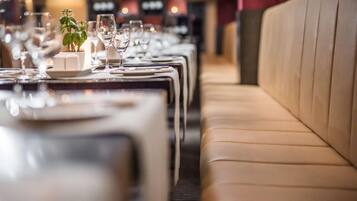 A row of tables with empty plates and glasses, a potted plant, and a beige booth in a restaurant.
