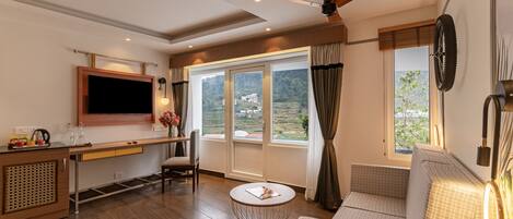 A modern living room with a sofa, a round coffee table, a TV mounted on the wall, and a large window with curtains.
