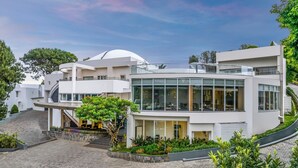 Un edificio moderno de varios pisos con fachada de vidrio curvo, área de estar al aire libre y una escalera que conduce a un nivel superior.