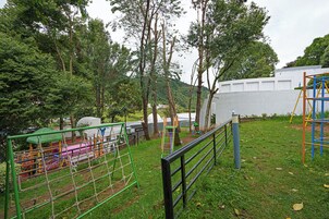 A playground with various play structures, surrounded by trees and a white wall.