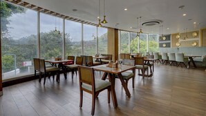 Un comedor amplio con mesas y sillas de madera, ventanas grandes que ofrecen vistas al exterior e iluminación colgante.