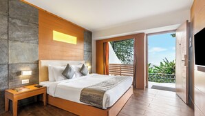Habitación de hotel moderna con cama de madera, mesita de noche, televisor integrado y balcón con vistas a zonas verdes.