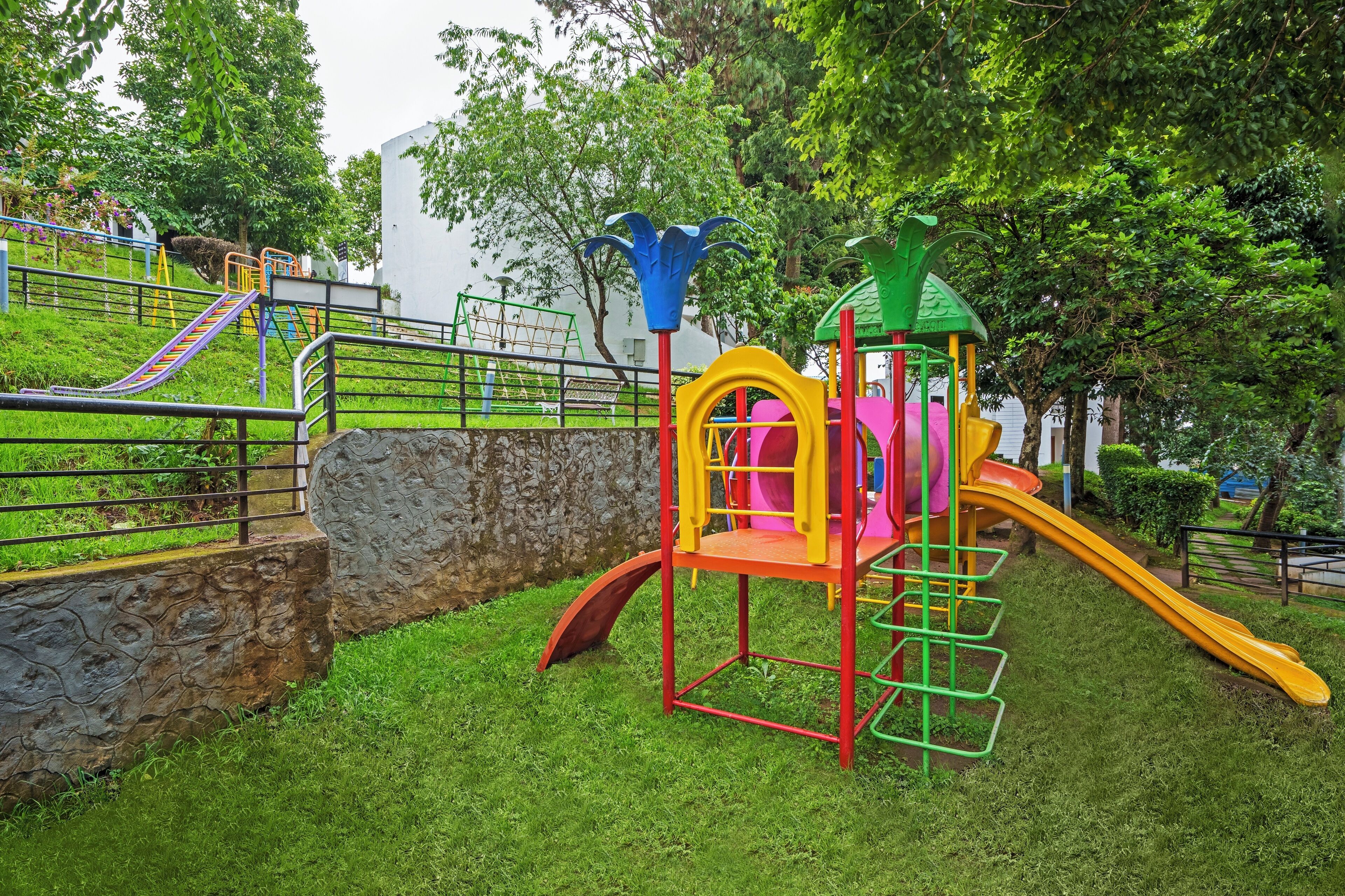 A playground with slides and climbing structures, surrounded by grass and trees.