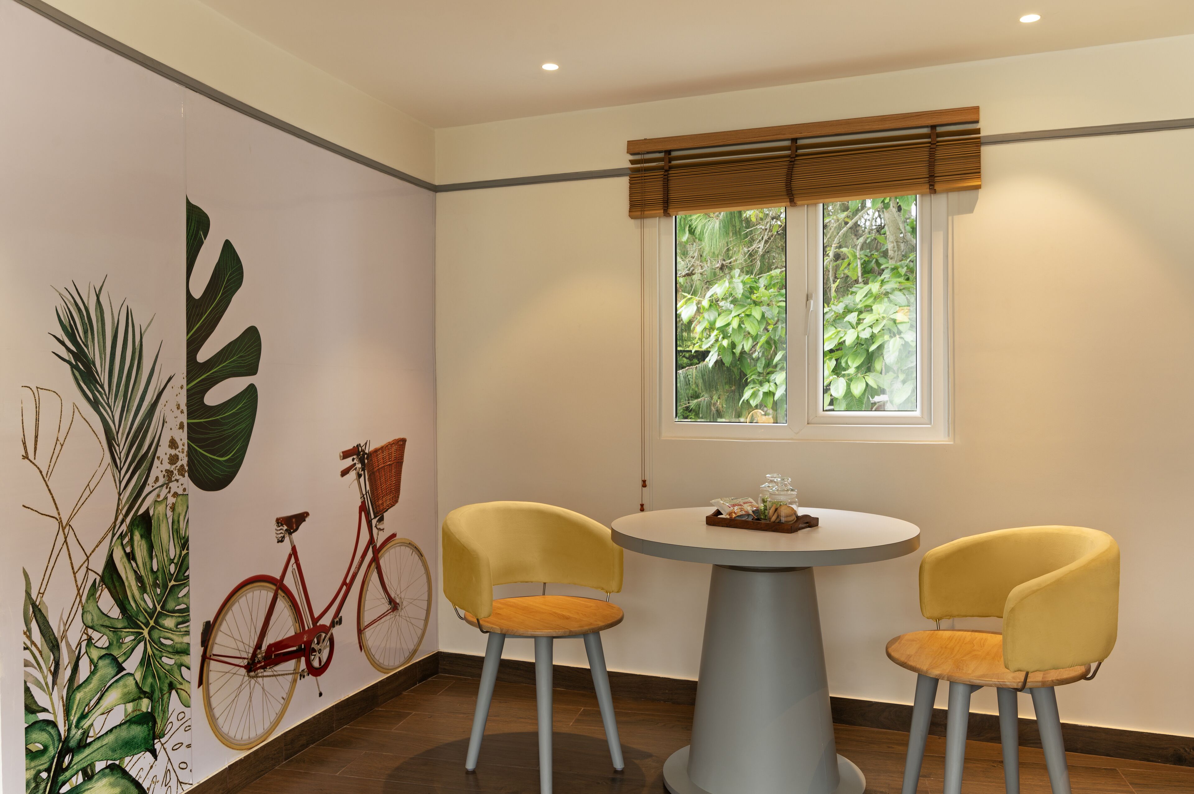Un comedor con una mesa redonda, dos sillas amarillas, una bicicleta roja y una ventana con vistas a zonas verdes.