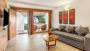 Una sala de estar moderna con un sofá, una mesa de centro con flores, un televisor y un balcón con vistas al verdor.