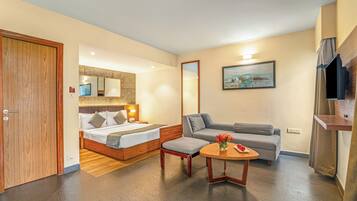 Ein Hotelzimmer mit Holztür, einem Bett mit Kopfteil, einem grauen Sofa, einem kleinen Tisch mit Blumenvase und einem Bild an der Wand.