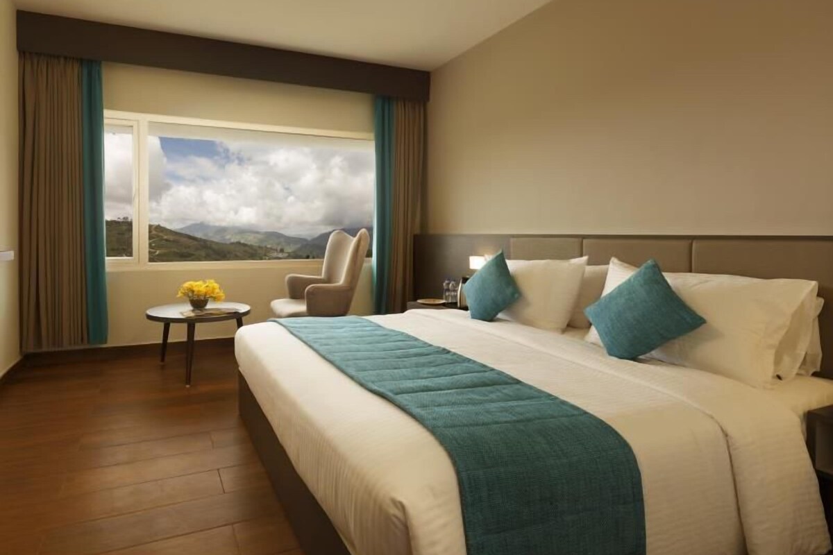 Habitación de hotel con una cama grande, una silla, una mesita y una ventana con vistas a la montaña.