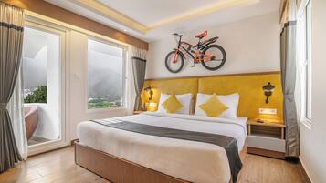 Habitación de hotel con una cama grande, una bicicleta colgada en la pared, vistas a la ciudad y una puerta corredera al exterior.