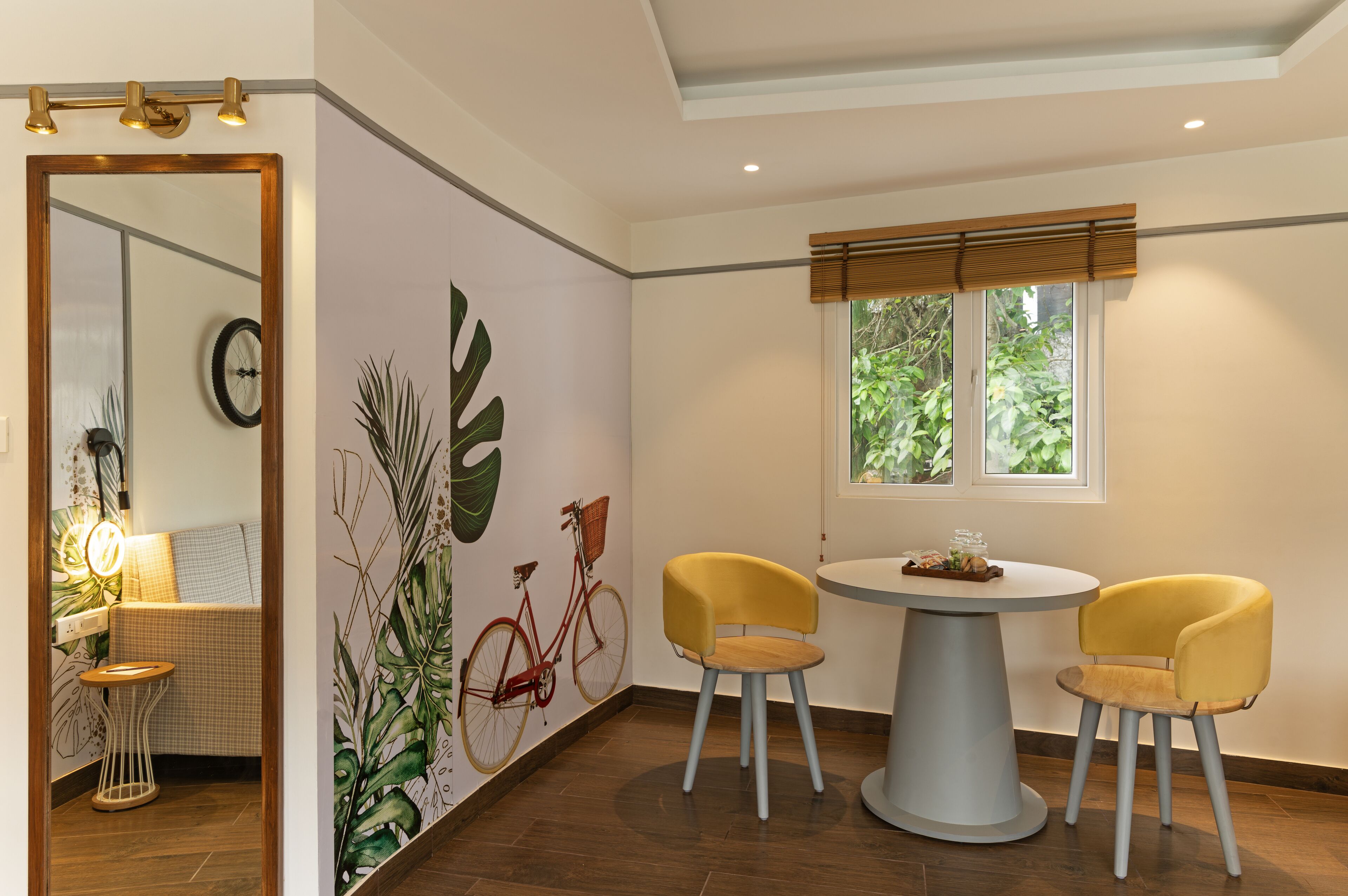 Un comedor con una mesa redonda, dos sillas amarillas, un espejo y una pared con un mural de una bicicleta.