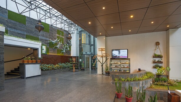 Un vestíbulo amplio con diseño moderno, que incluye un mostrador de recepción, una escalera y diversas plantas en macetas.