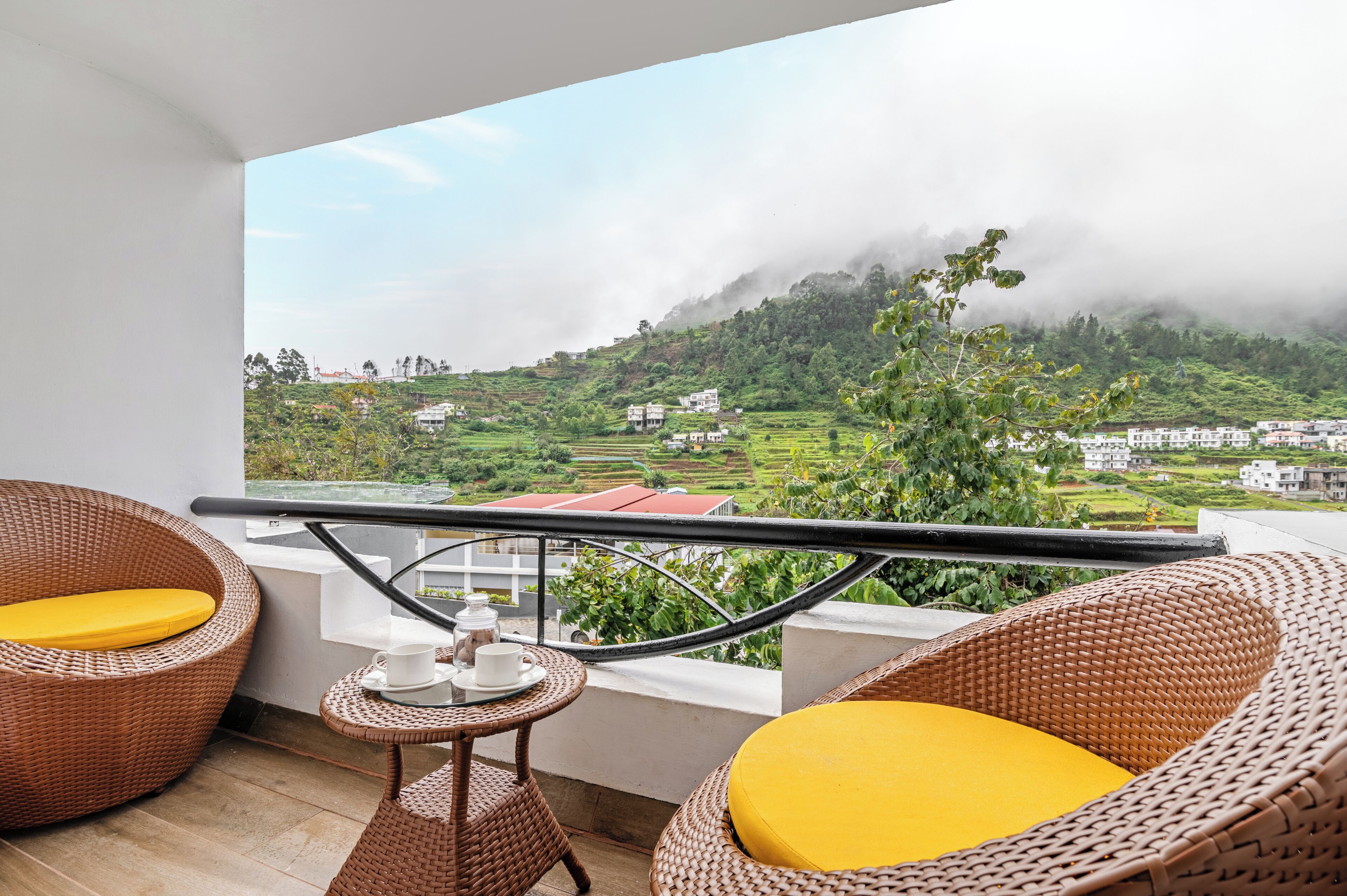 A balcony with wicker furniture and a view of a green landscape with buildings.