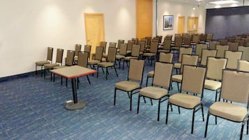 A conference room with rows of chairs and tables, a projector screen, and a door in the background.