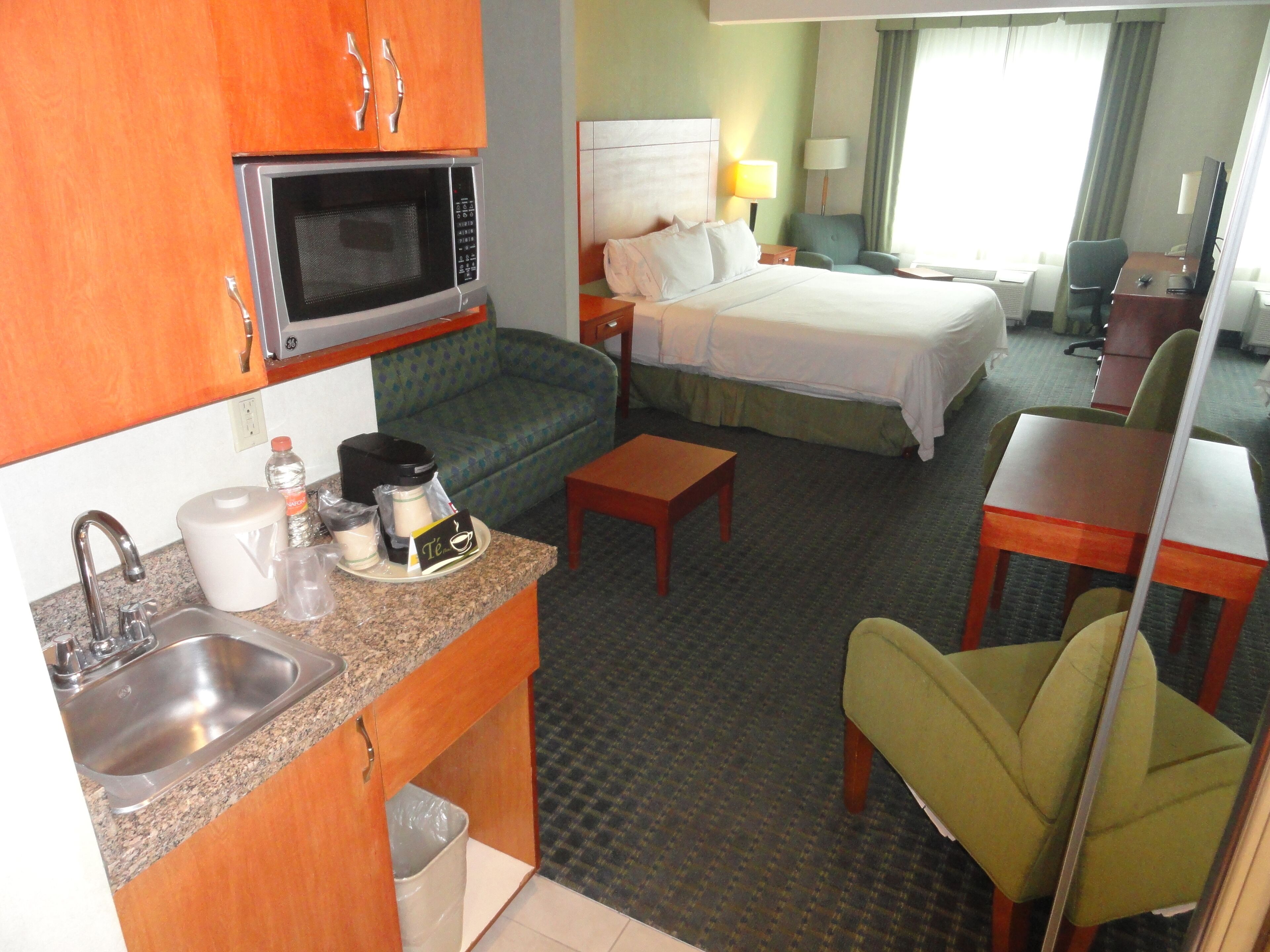 Ein Hotelzimmer mit Küchenzeile, einem Bett, einer Couch, einem Schreibtisch und einem Stuhl.