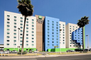 Ein mehrgeschossiges Hotel mit einem Holiday Inn Express & Suites Schild, das ein modernes Design mit einer Kombination aus weißen und blauen Fassaden sowie Palmen vor der Fassade zeigt.