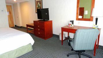 A hotel room with a bed, a desk with a chair, a television, and a small table with a coffee maker.