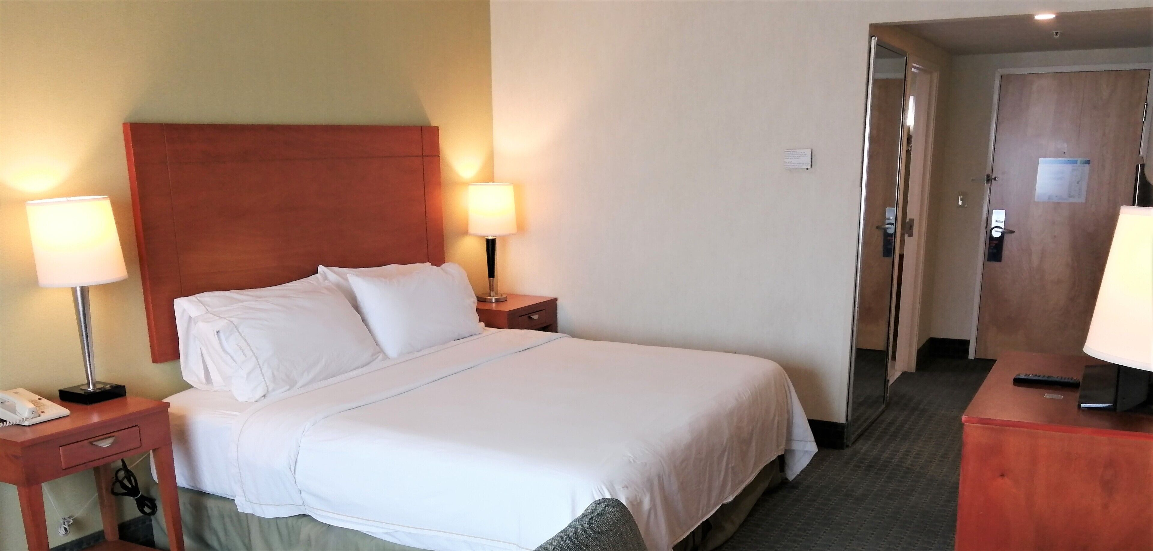 Una camera d'albergo con un letto grande, due abat-jour, una testiera in legno e una scrivania con lampada.
