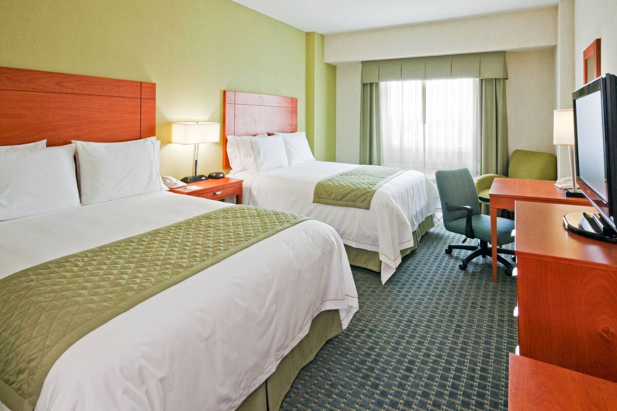 A hotel room with two beds, a desk, a chair, a television, and a window with curtains.