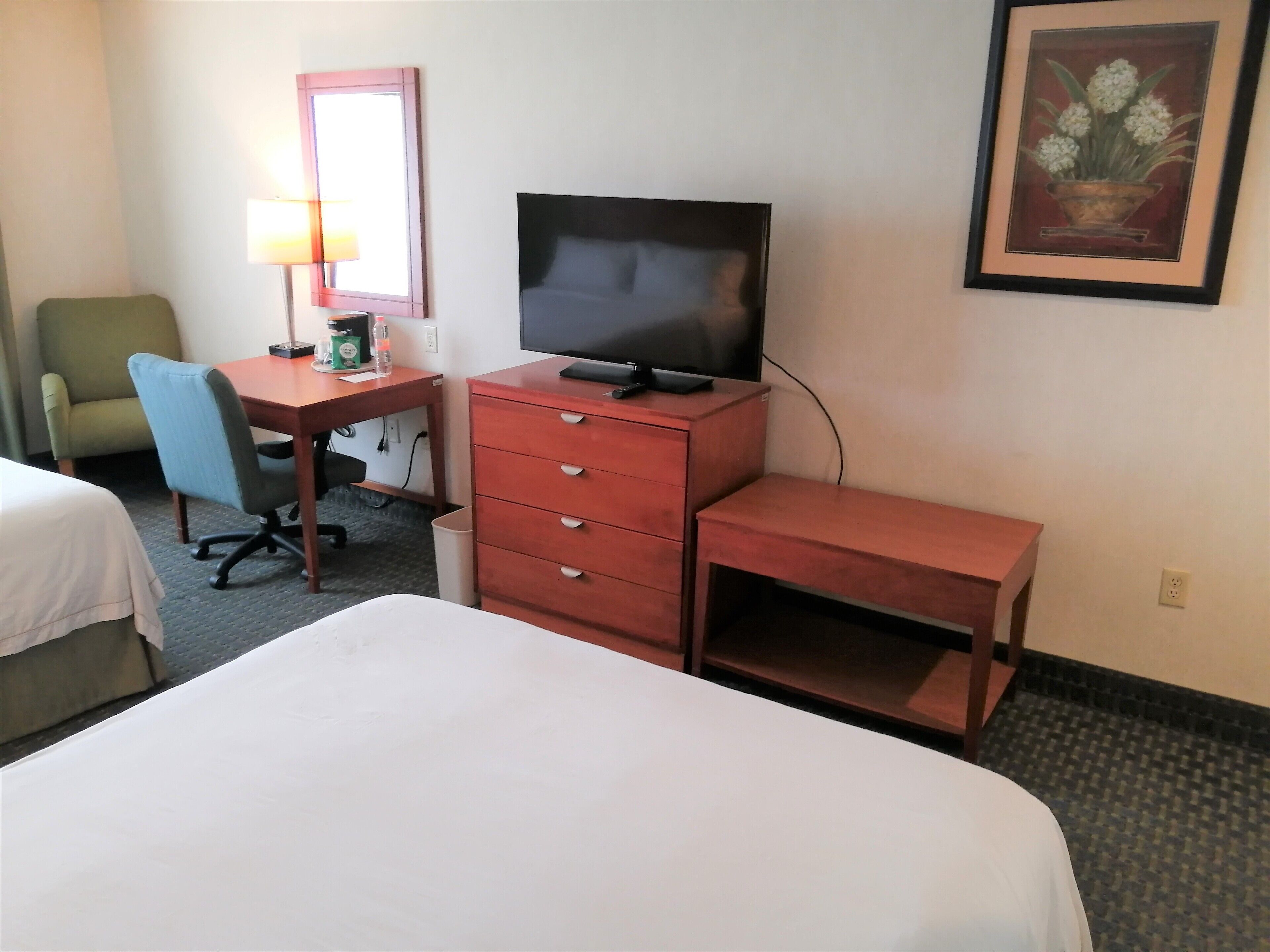 A hotel room with a bed, a desk with a computer, a chair, a television, and a framed picture on the wall.