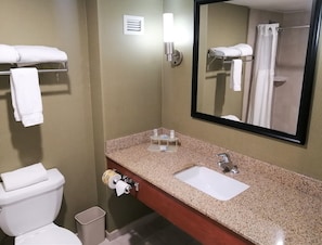 Un baño con inodoro, lavamanos, espejo, toallero y un cubo de basura.