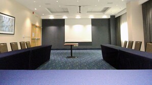 Un salón de conferencias con una larga mesa, sillas, una pantalla de proyector e iluminación empotrada en el techo.