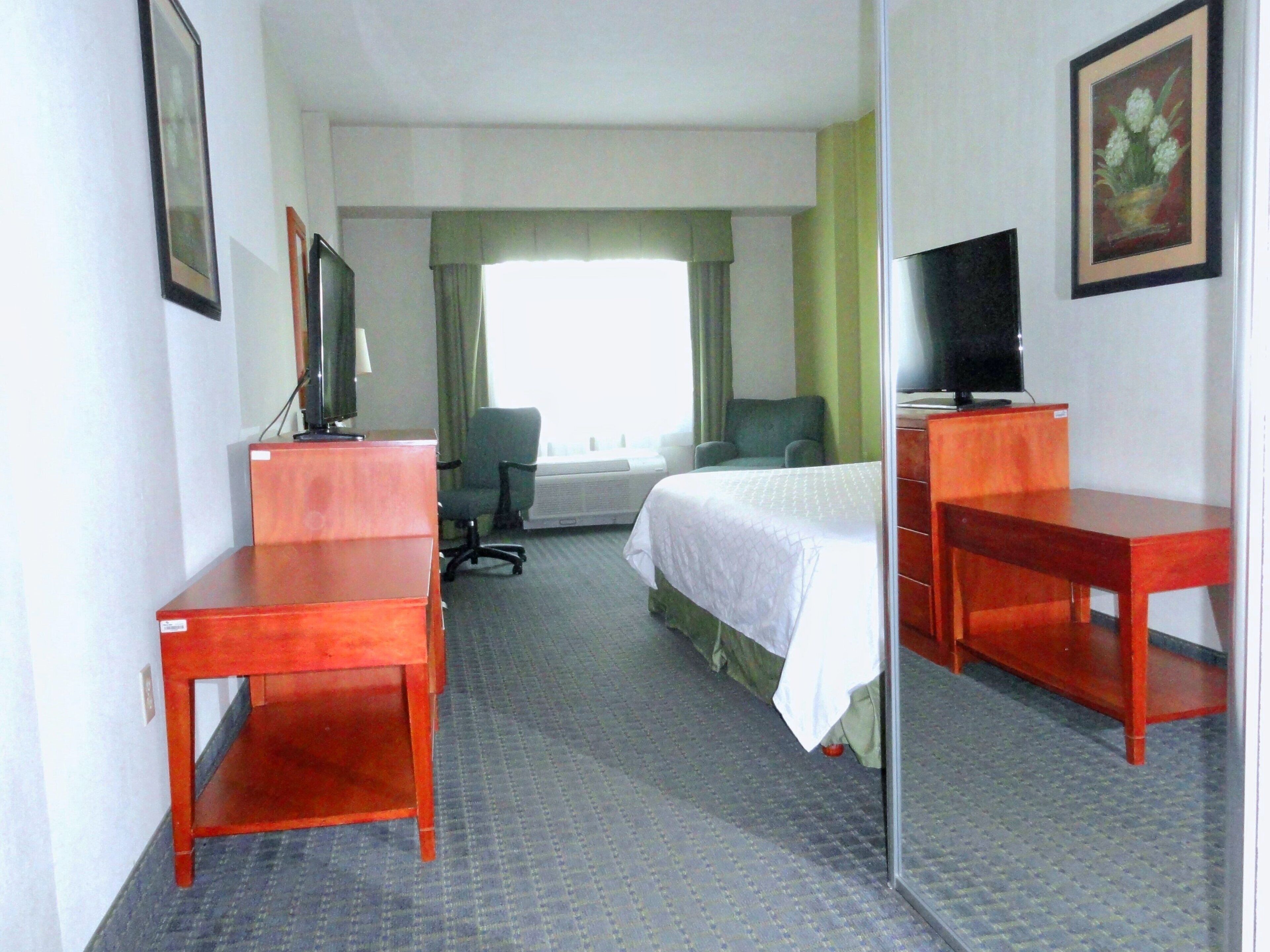 Habitación de hotel con cama, escritorio, silla, televisor y ventana con cortinas.