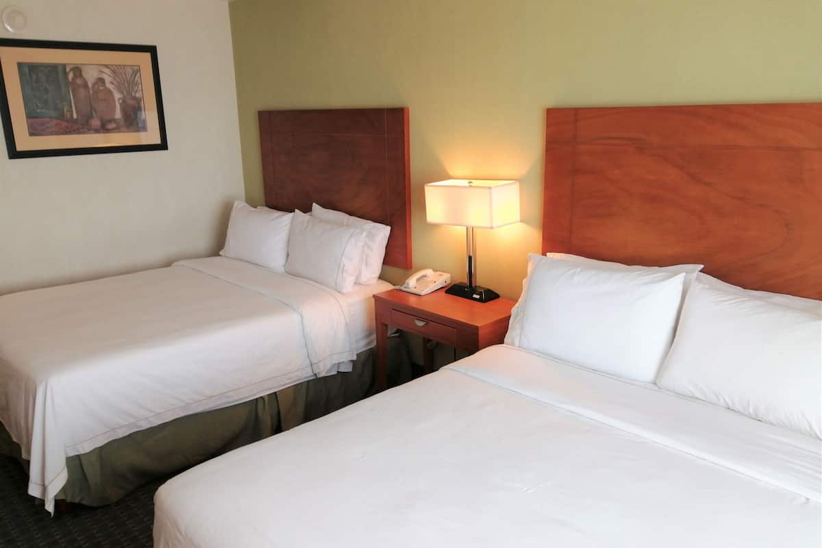 A hotel room with two single beds, a nightstand with a lamp, and a painting on the wall.