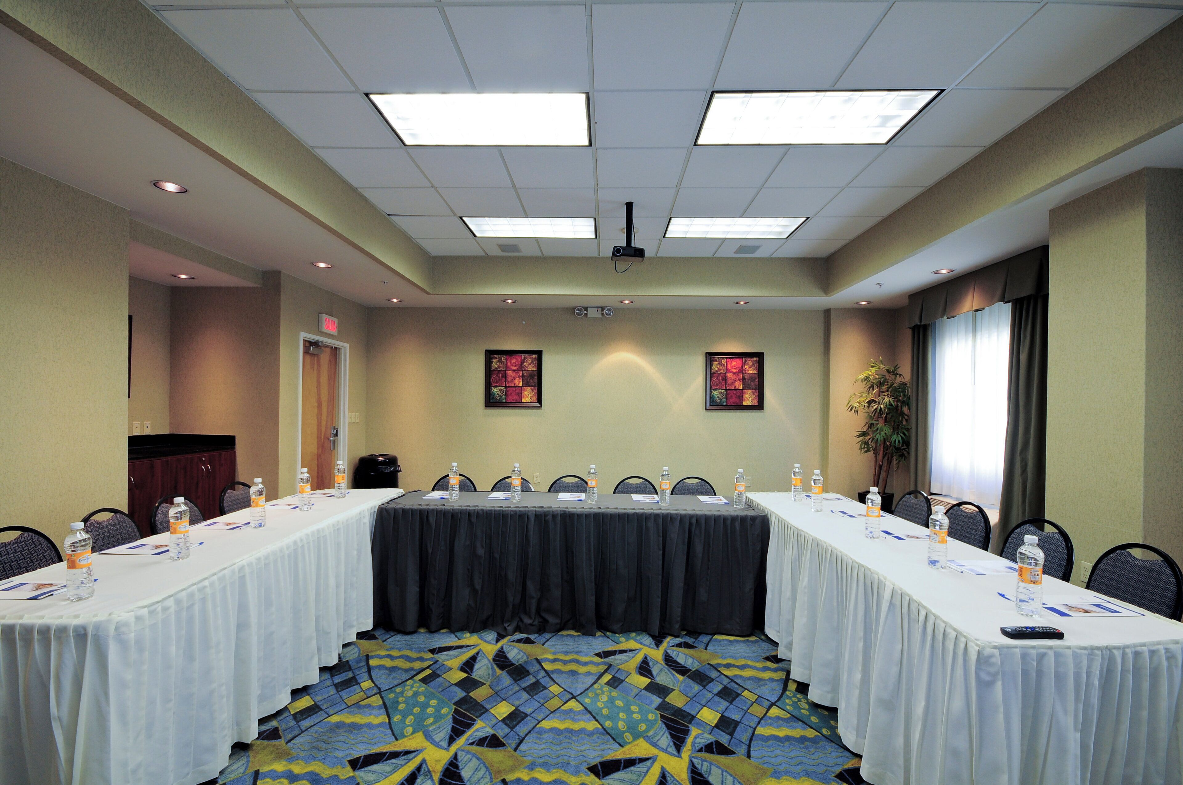 A conference room with a long table, chairs, water bottles, and a projector screen.