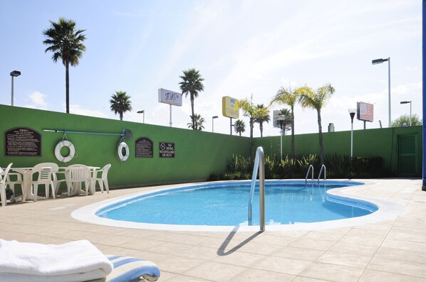 Una piscina con pared verde, palmeras y un puesto de socorrista.