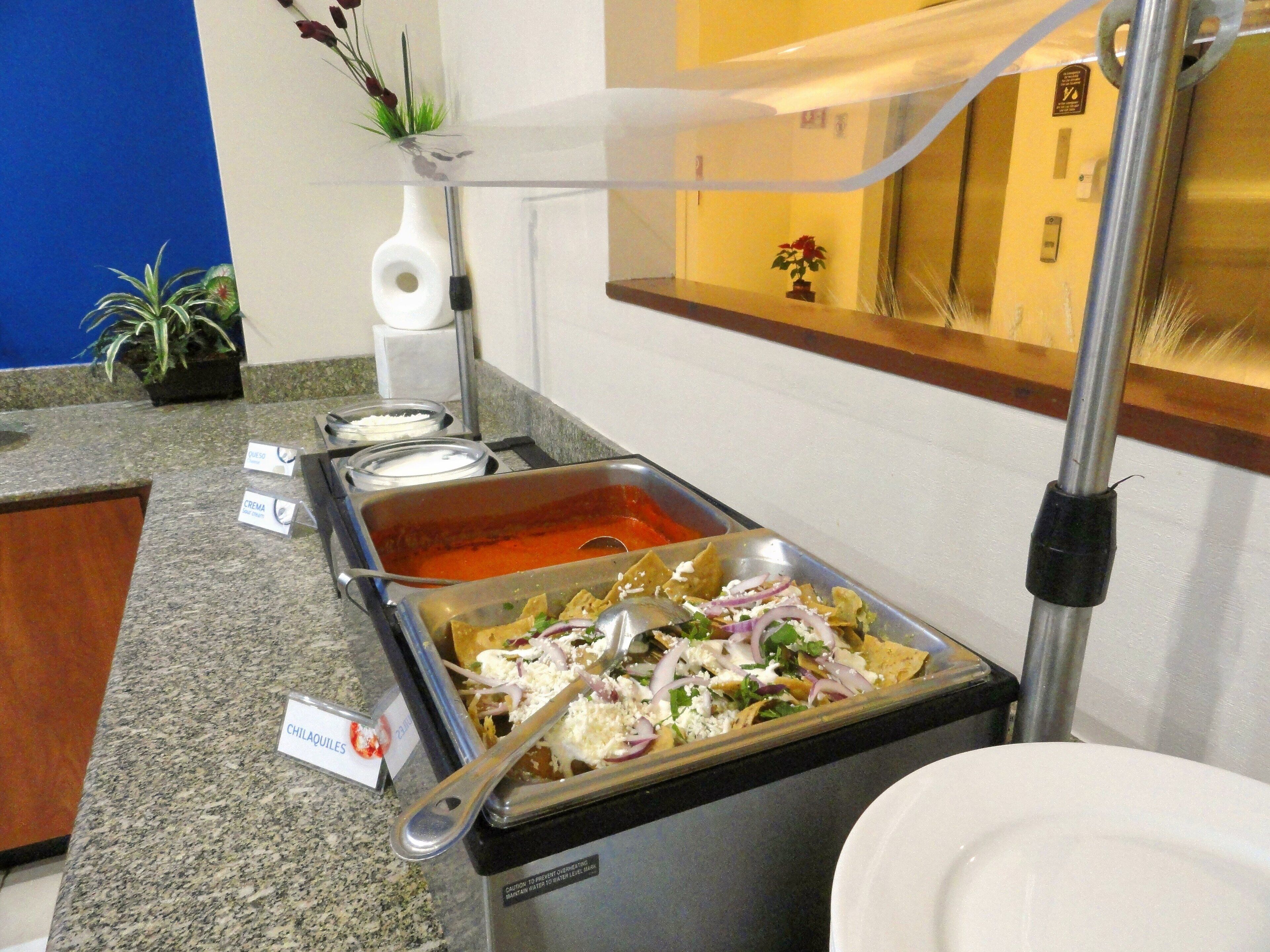 A buffet area with a variety of food options including a hot sauce, a cheese dish, and a tray of nachos.