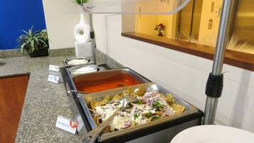 A buffet area with a variety of food options including a hot sauce, a cheese dish, and a tray of nachos.