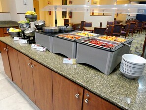 Un espace buffet avec des récipients étiquetés contenant du granola, du yaourt et des fruits.