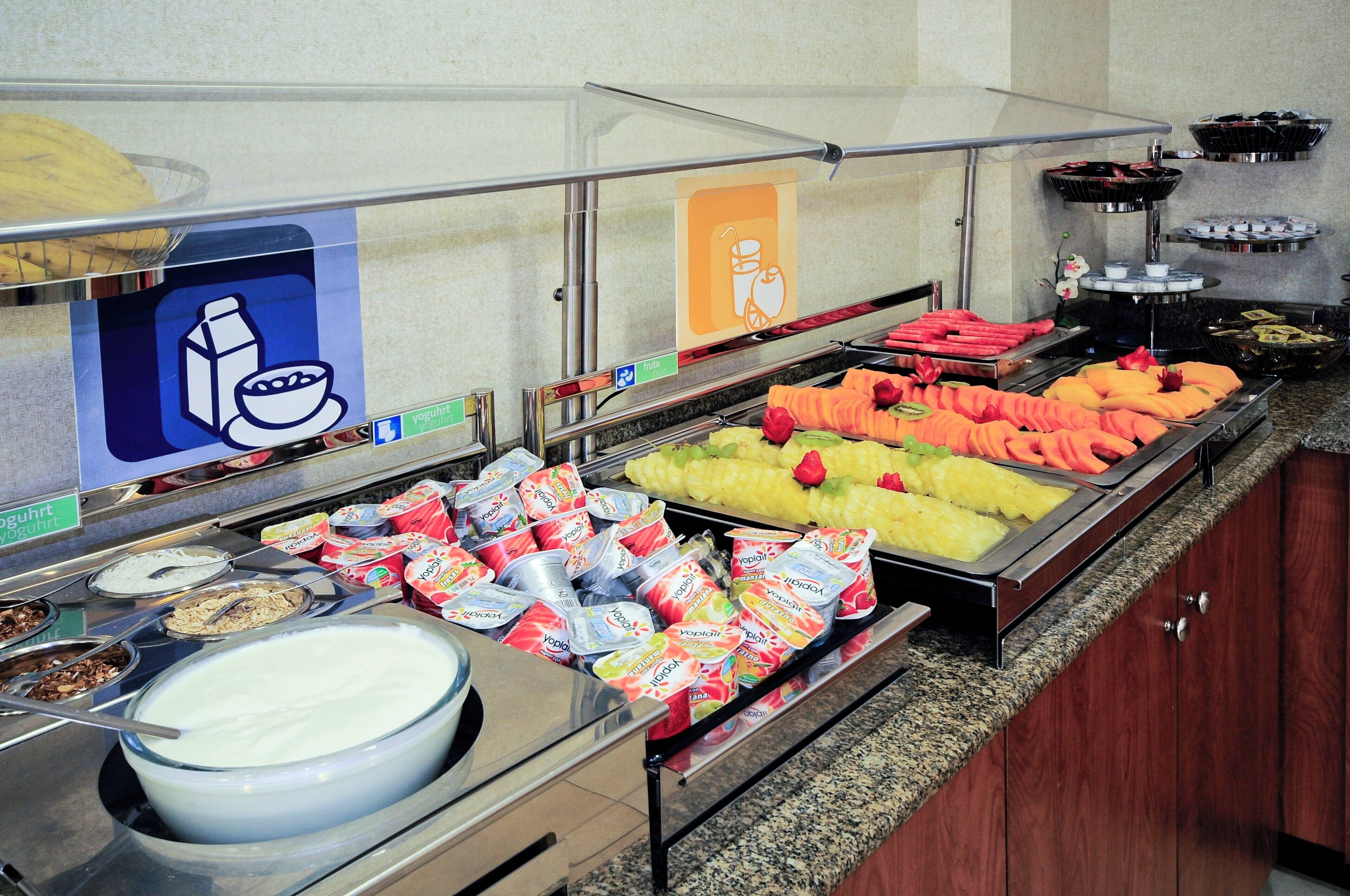 Un bufé con diversas opciones de comida, incluyendo frutas, yogur y cereales.