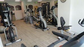 Un gimnasio con diversas máquinas de ejercicio, un reloj en la pared y suelo alfombrado.