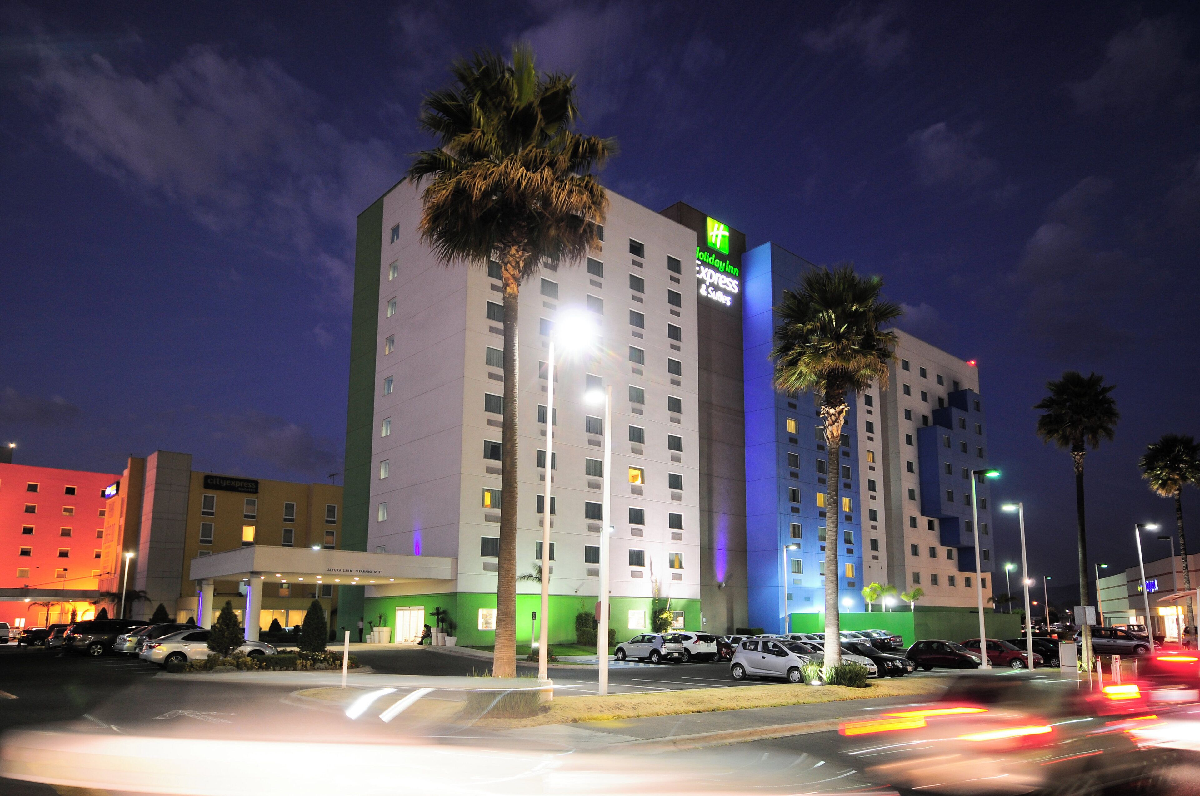 A multi-story hotel with a Holiday Inn Express sign, a parking lot with cars, and palm trees.