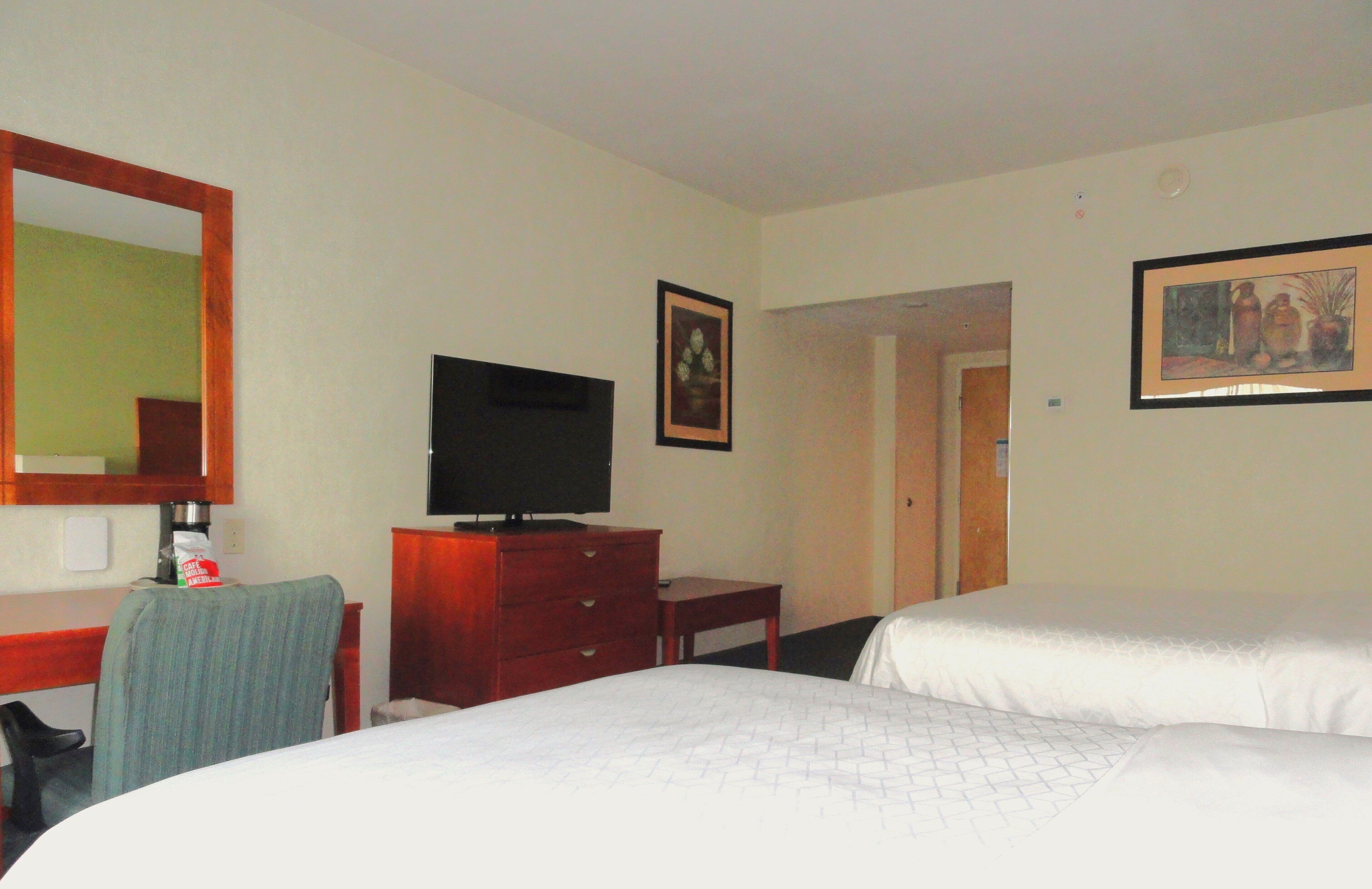 Ein Hotelzimmer mit einem Bett, einem Schreibtisch mit Fernseher, einem Sessel und einer Kommode.