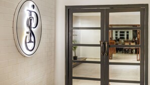 A door with a glass panel and a metallic sign with a letter 'D' on a white brick wall.