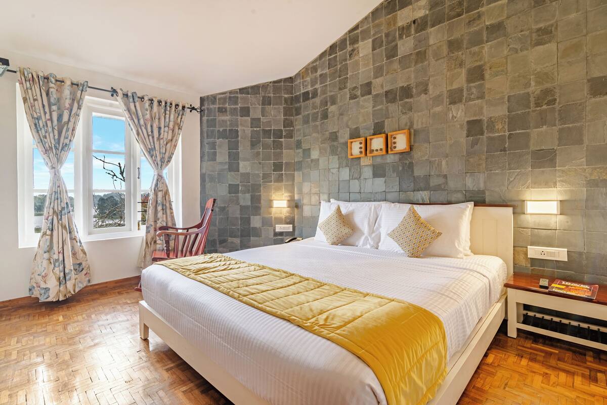 Une chambre avec un grand lit, un plancher en bois, un mur en pierre et une fenêtre avec des rideaux.