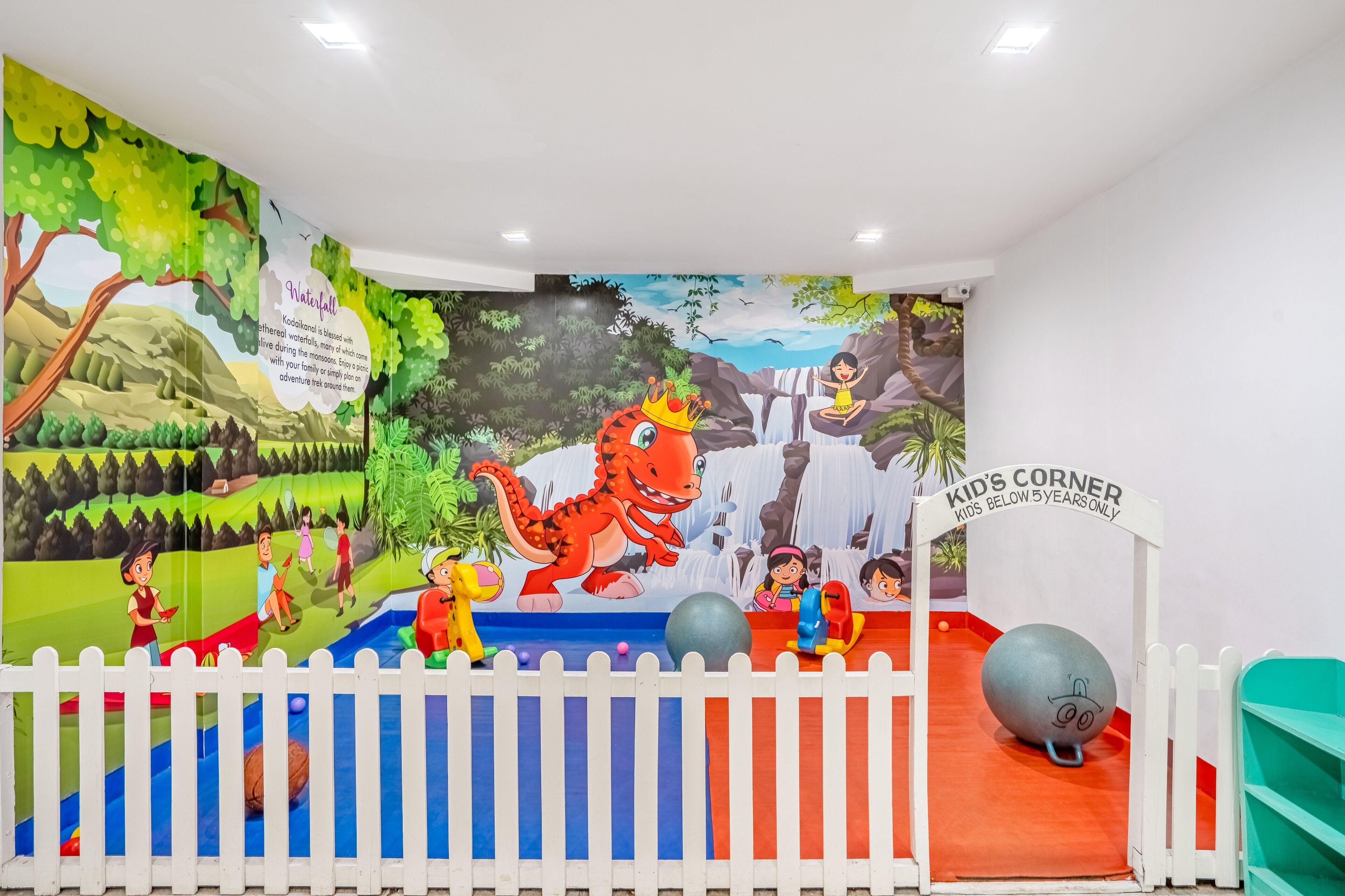 A children's play area with a mural, a white picket fence, and exercise balls.