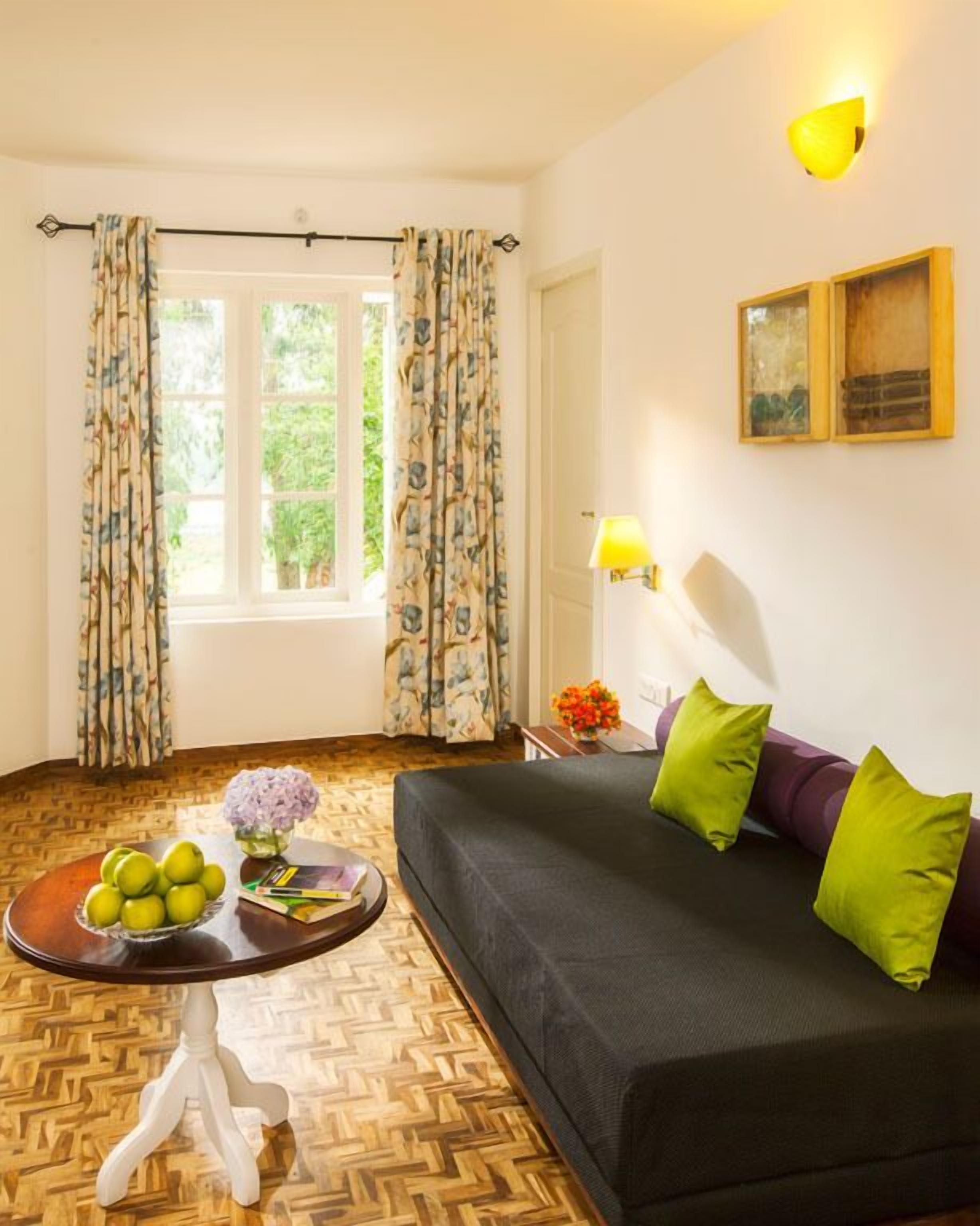 Una habitación con sofá, una mesita con un frutero, una lámpara y una ventana con cortinas.