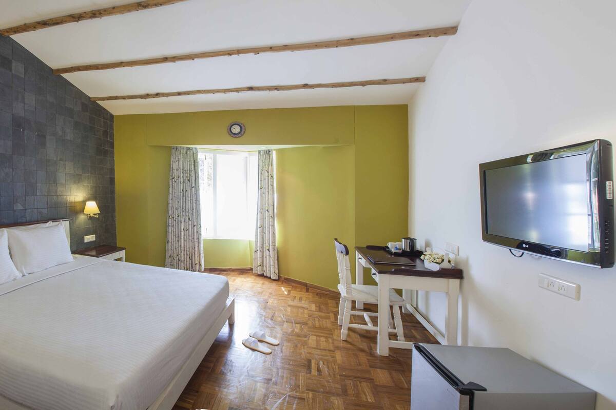 Une chambre d’hôtel avec un lit, un bureau, une télévision et une fenêtre avec des rideaux.