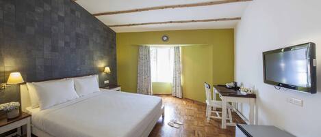 A hotel room with a bed, a desk, a TV, and a window with curtains.