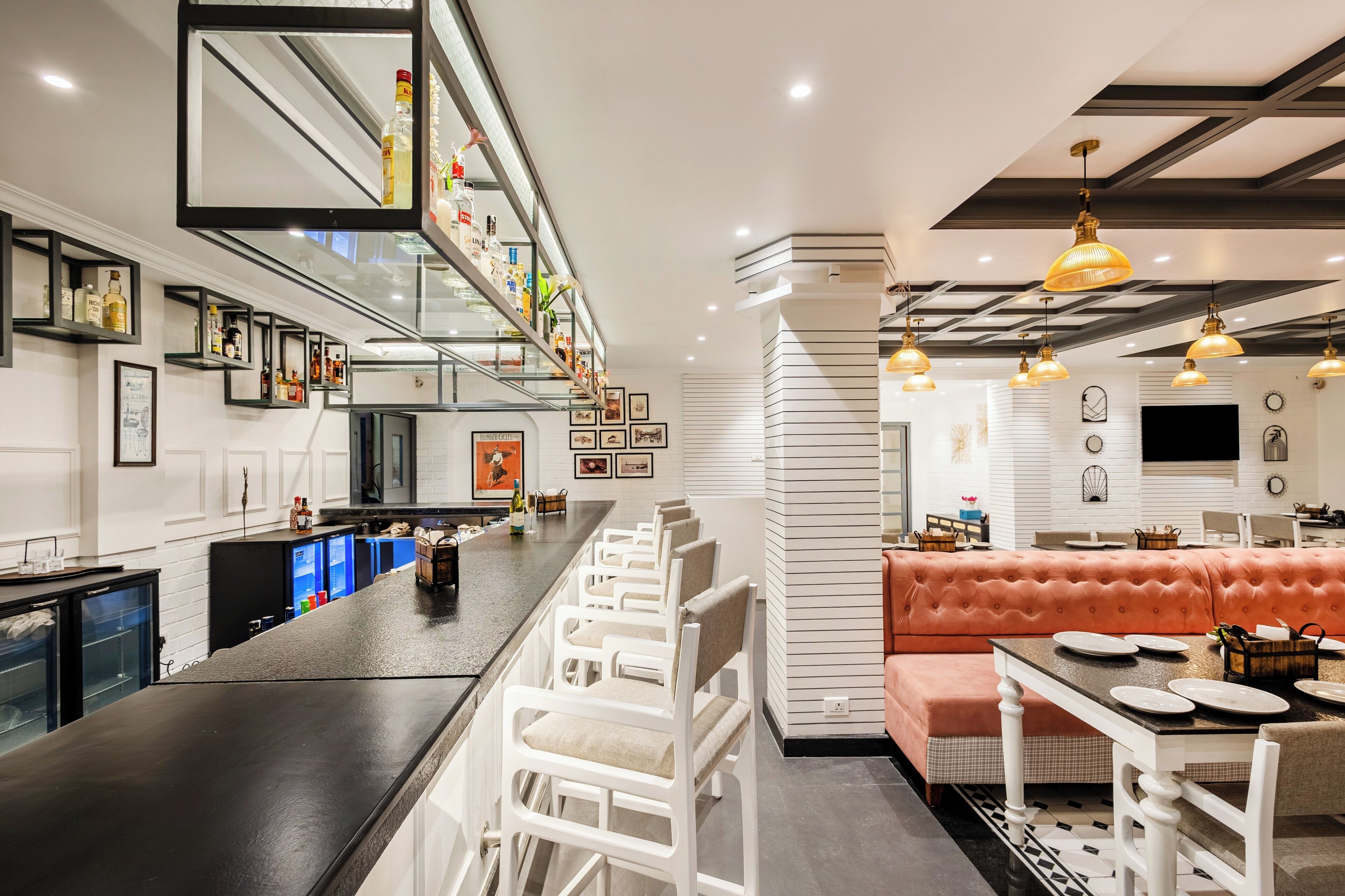 Una cocina moderna con barra, taburetes blancos, sofá rosa e iluminación colgante.