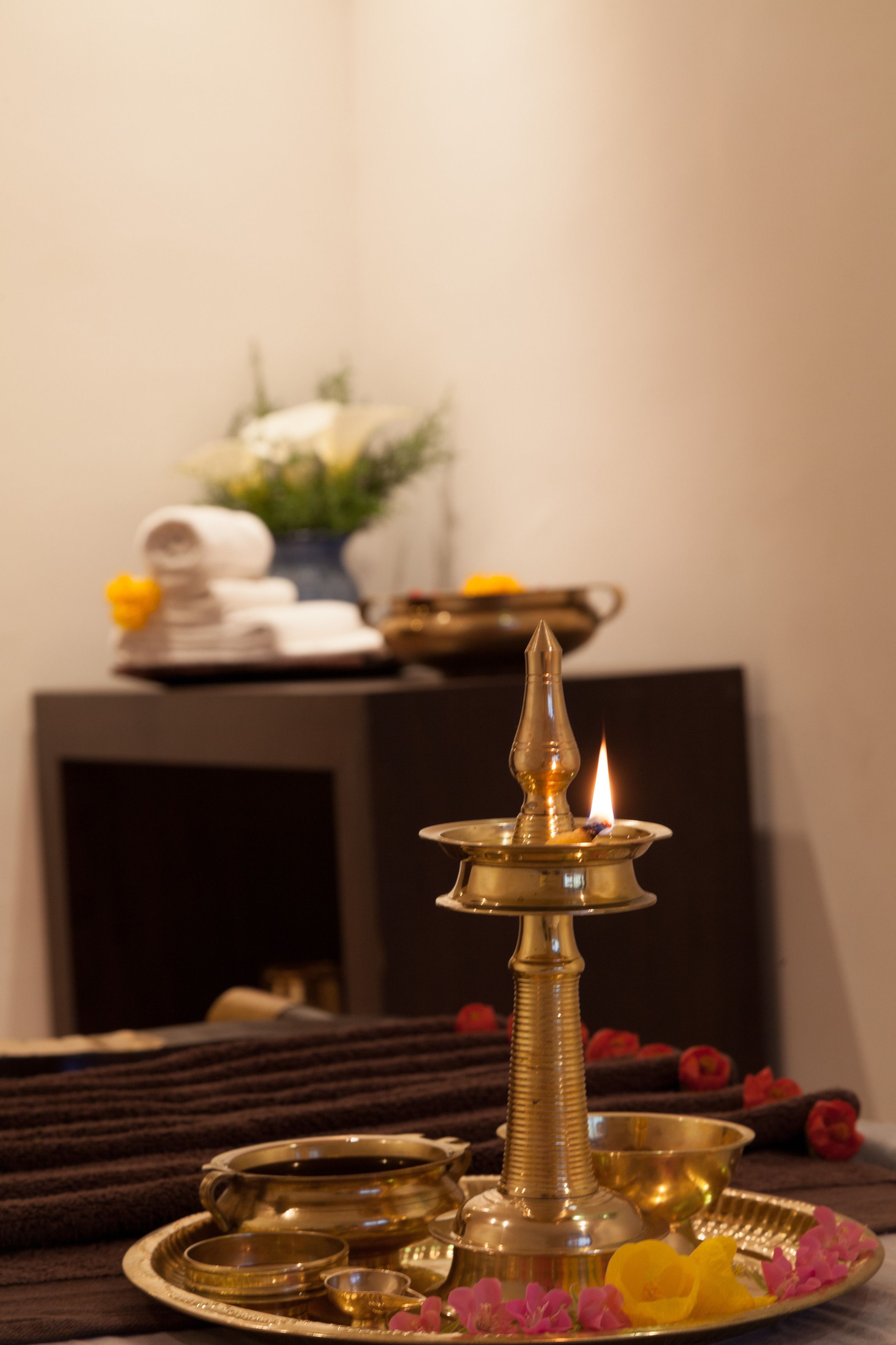 A brass oil lamp with a lit candle on a tray with small bowls and a flower.
