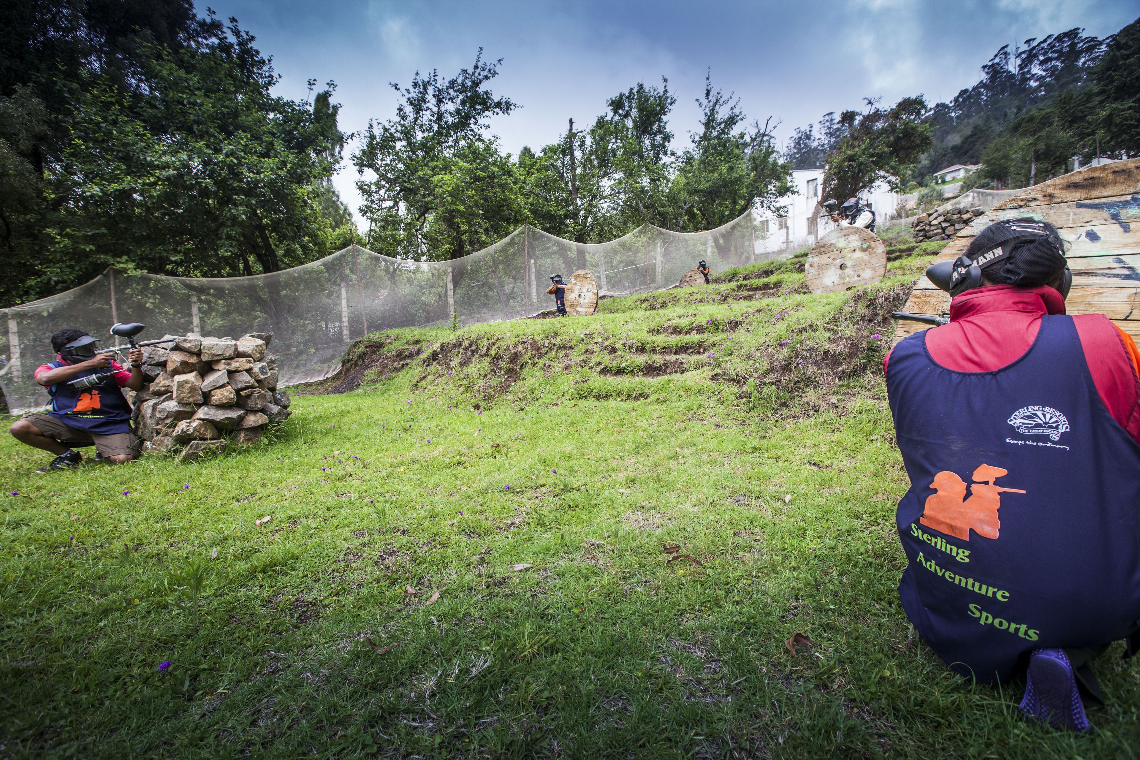 A paintball game in an outdoor setting with netted barriers and a grassy field.