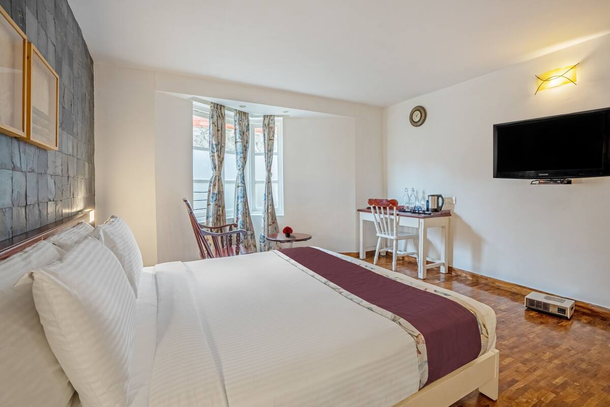 Une chambre d’hôtel avec un lit, un bureau, une chaise, une télévision et une fenêtre avec des rideaux.