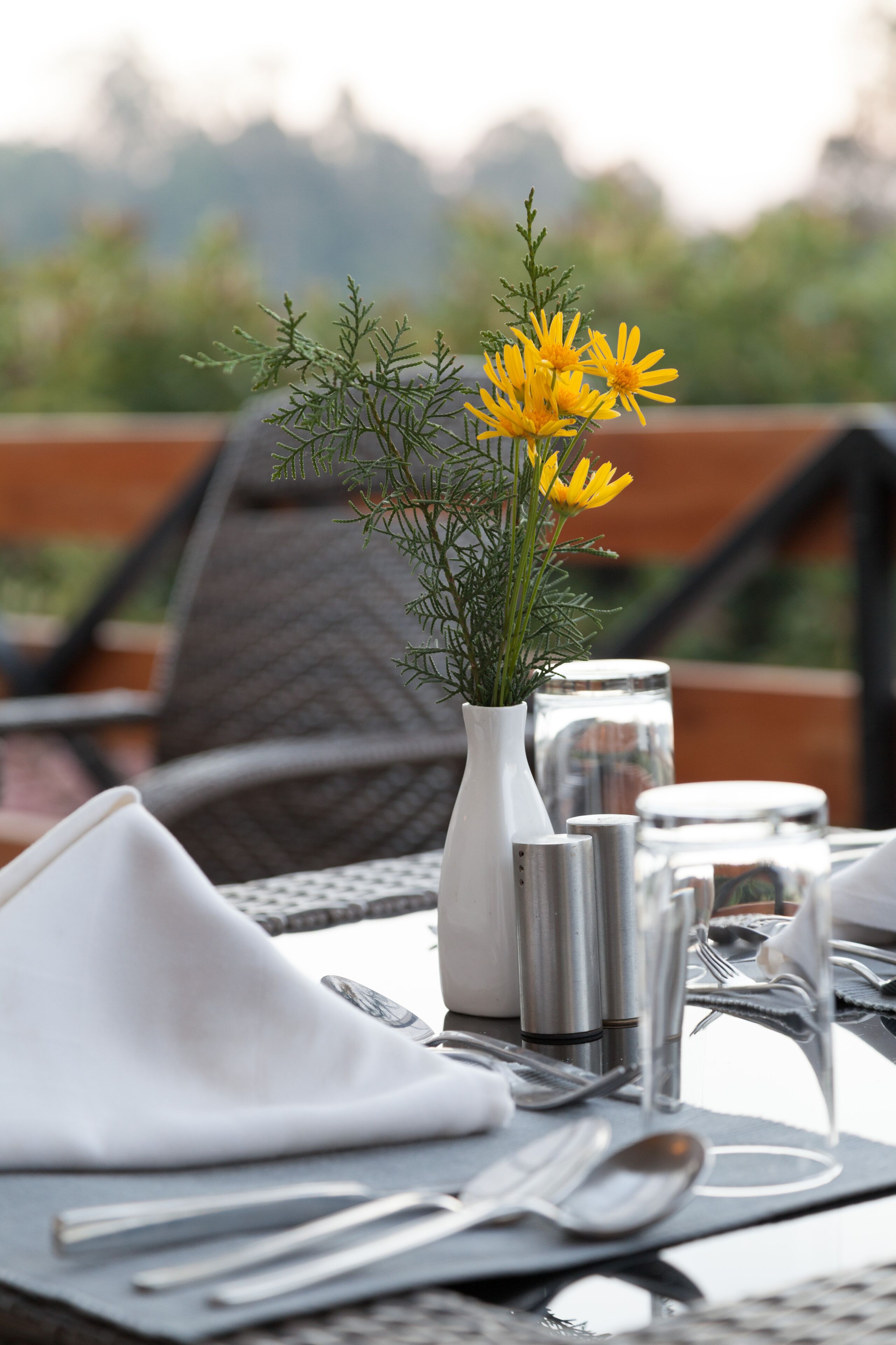 A table set for dining with a white napkin, silverware, and a vase with yellow flowers.