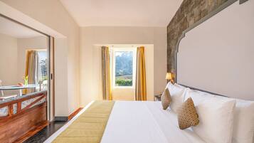 A hotel room with a bed, a desk, a chair, a window with curtains, and a view of greenery outside.