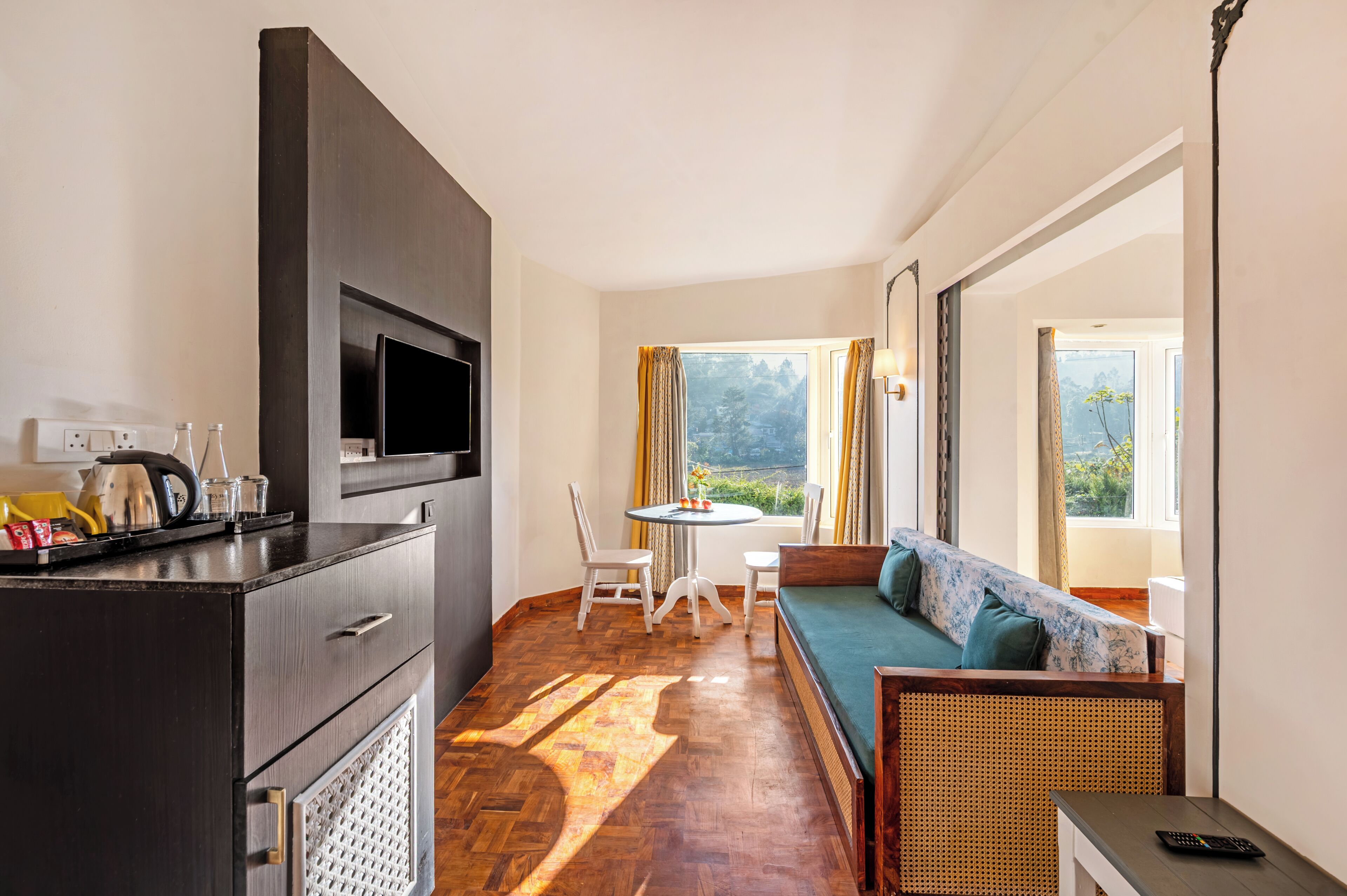 A room with a sofa, a dining table with chairs, a TV mounted on a cabinet, and a window with curtains.