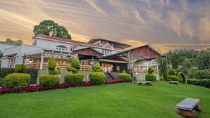 A hotel with a well-maintained lawn, neatly trimmed hedges, and a large tree in the background.